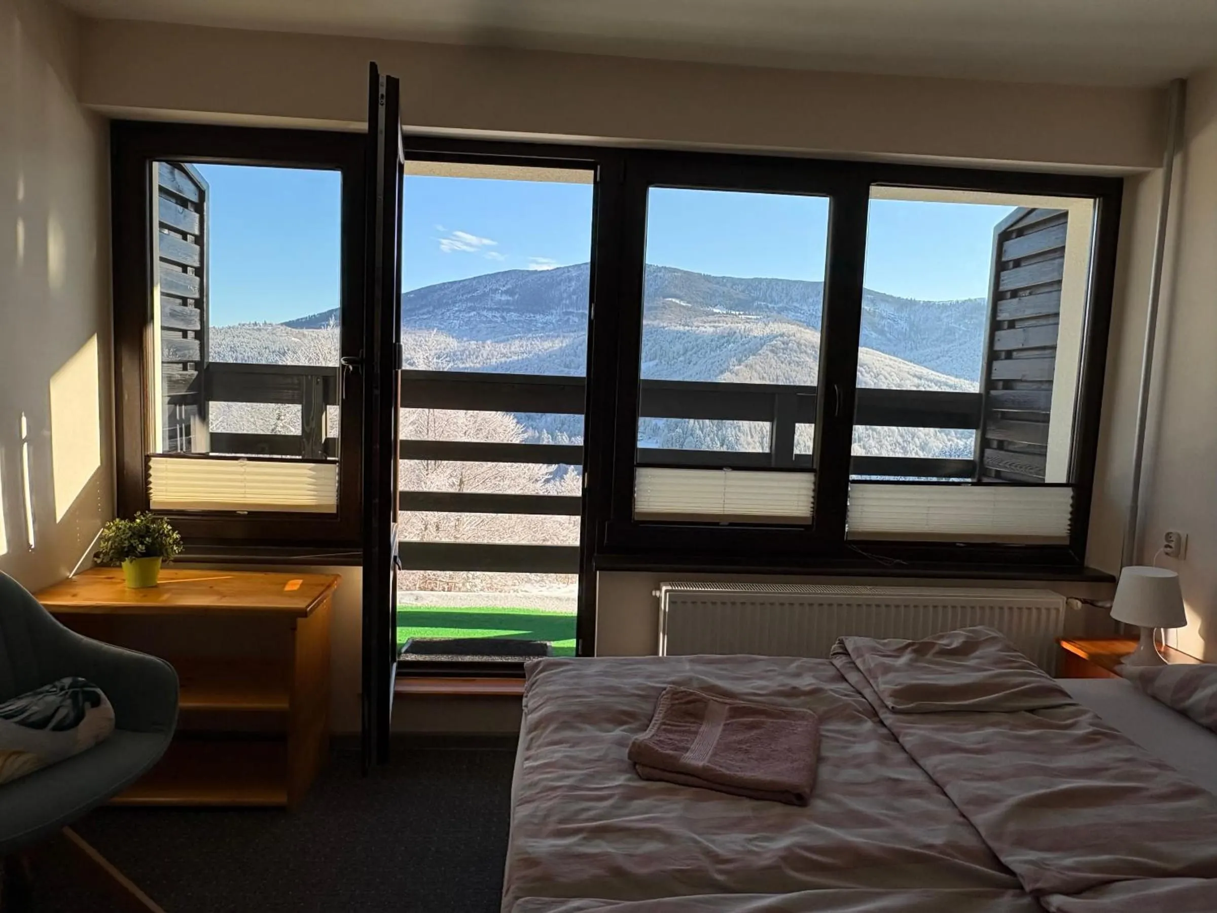 Pokój z dwoma zsuniętymi łóżkami i otwartymi drzwiami na balkon, za oknem zaśnieżone góry